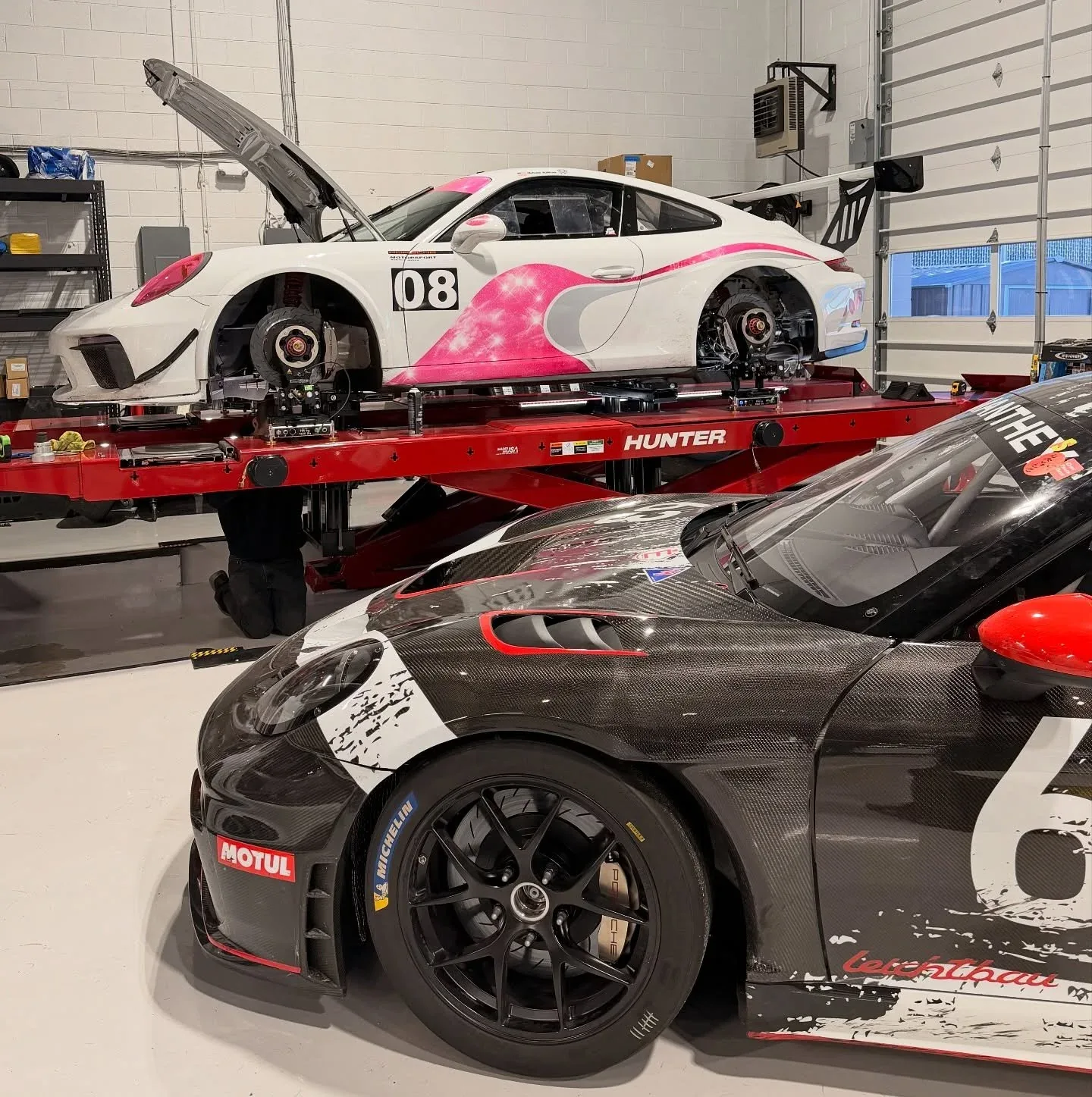 A Porsche Cayman raised on the Hunter alignment rack beside a carbon-bodied Manthey 718 GT4