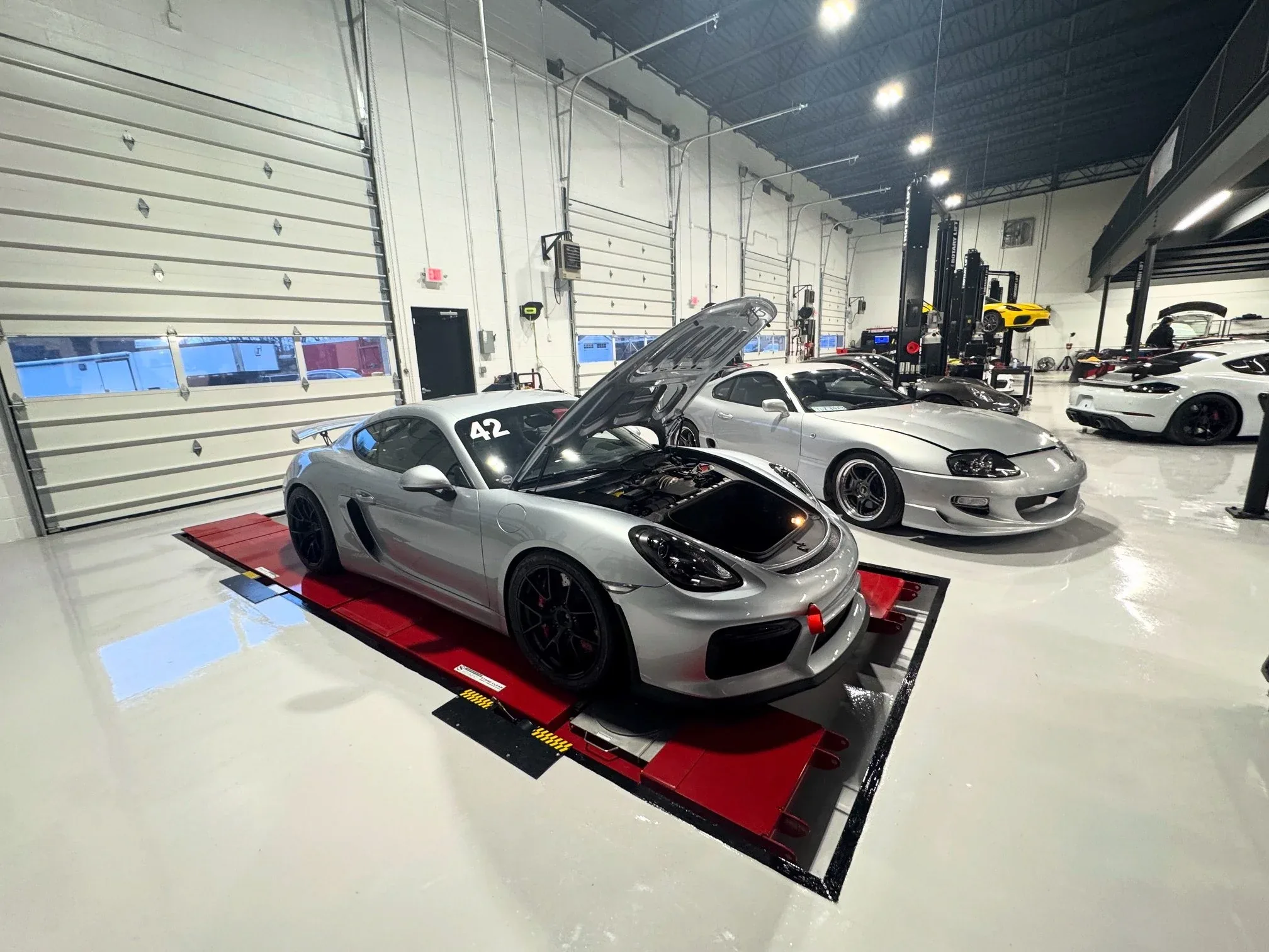 A silver Porsche 718 Cayman GT4 on the alignment ramps in the Red Beard Racing workshop